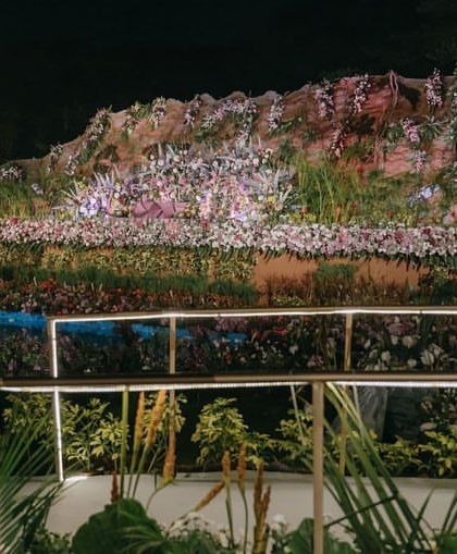 A side view of the reception stage, offering a glimpse of the detailed rock formations and the sheer volume of flowers used to create this naturalistic yet fantastical landscape.