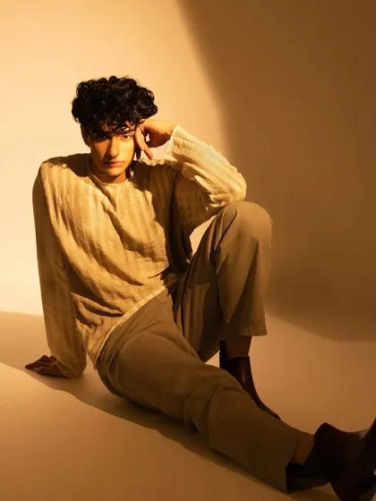 A seated pose under warm lighting. The makeup ensures his skin looks even and free of shine.