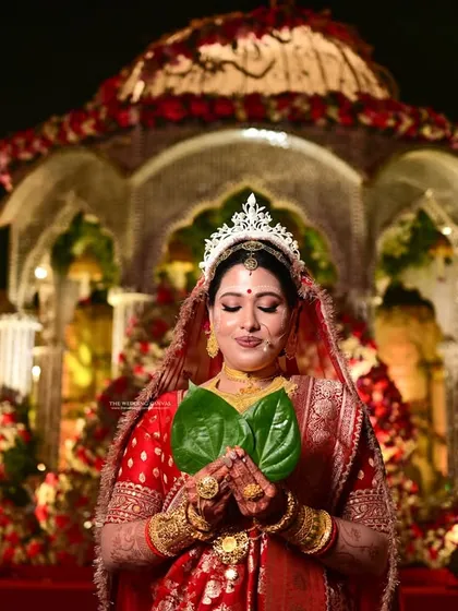 The bride takes center stage during the wedding rituals. This shot captures her holding the paan pata against the backdrop of the beautifully decorated mandap, a key moment in the ceremony.