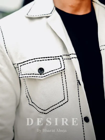 A close-up of the contrast stitching on the all-white jacket. This detail highlights the craftsmanship and adds a modern, graphic touch to the minimalist design.