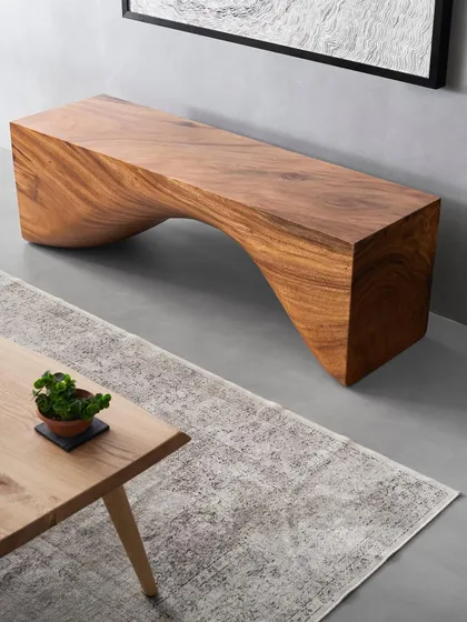 A detailed shot of the East Indian walnut bench. The design explores the intersection of furniture and sculpture, creating a functional piece of art that serves as a focal point and a testament to the beauty of natural wood.