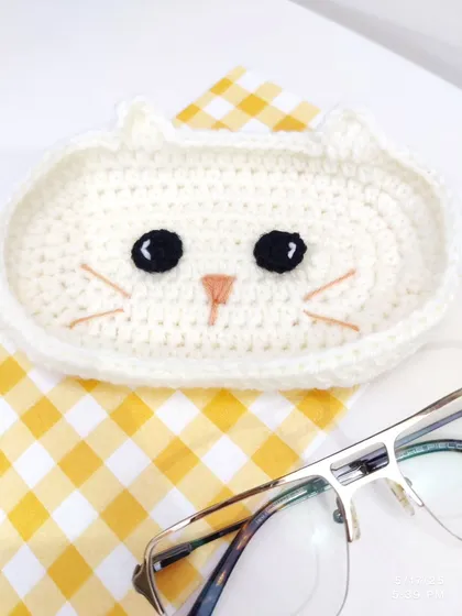 The cat dish next to a pair of glasses, showing its intended use as an eyeglasses holder.