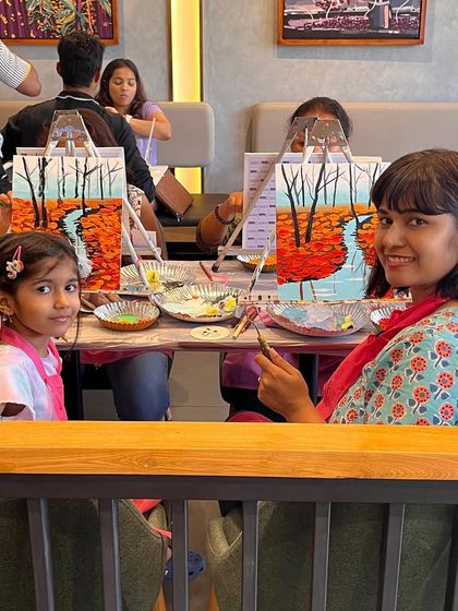 A mother and daughter painting side by side at a cafe workshop. It's a heartwarming sight and a great bonding activity.