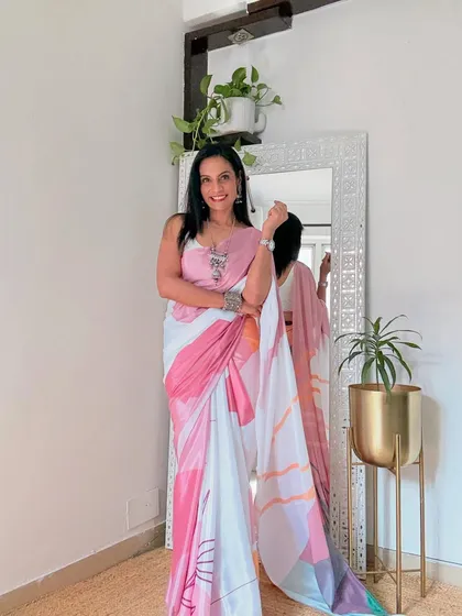 This abstract print satin saree in shades of pink and white is a modern and artistic choice for the workplace. The fabric is smooth and has a beautiful flow.