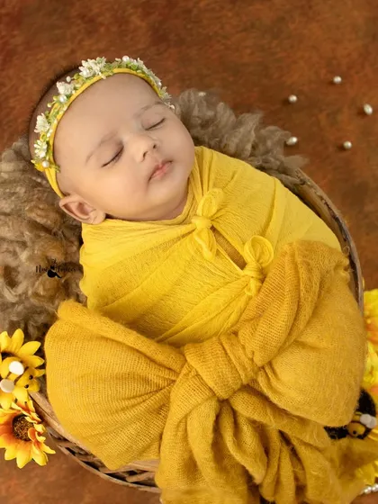 A ray of sunshine, this newborn is wrapped in a bright yellow swaddle and surrounded by sunflowers. This setup is perfect for a cheerful and vibrant baby announcement.