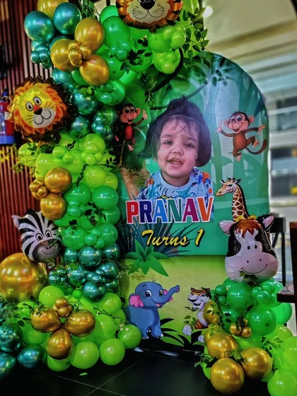 A personalized jungle theme welcome sign for a first birthday party. This setup features a custom poster with the child's photo, surrounded by a green and gold balloon arrangement with animal foil balloons.