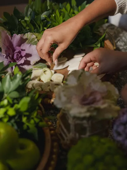 An intimate Mehendi setup where the focus was on the soul of greens. This close-up shows hands arranging a composition of lush foliage, rare leaves, and unexpected fruits, creating a celebration of nature that is both unorthodox and sophisticated.