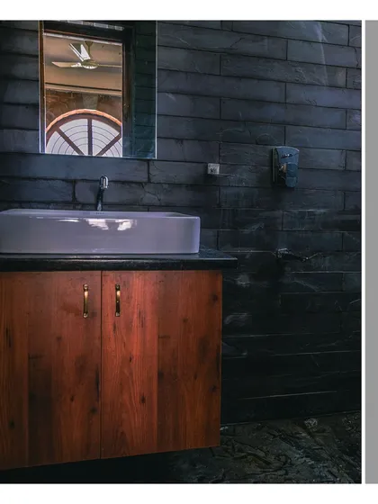 A bathroom vanity showing the contrast between the dark, rough texture of the slate wall and the warm, smooth finish of the wooden cabinet.