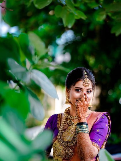 A similar pose from the same series, this time with a joyful and direct smile towards the camera. The natural framing by the leaves adds depth and a touch of spontaneity to this beautiful traditional portrait.