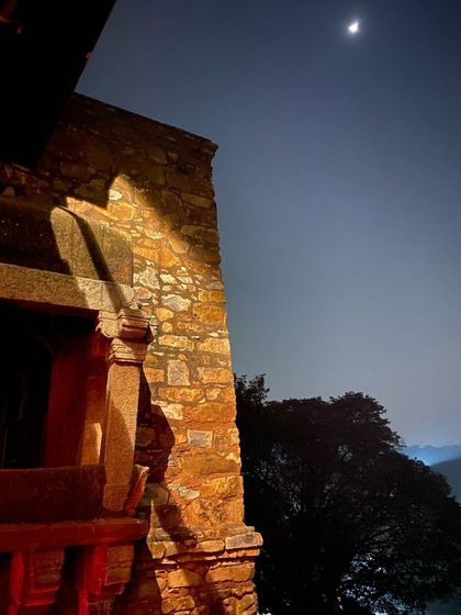 The ruins of Hauz Khas fort illuminated at night, with the crescent moon hanging in the sky above.