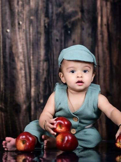 A baby boy sitting amidst red apples with a rustic wooden background.