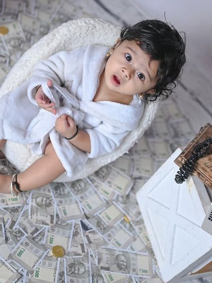 A wider shot of the 'Money' theme, showing the baby surrounded by prop currency and a vintage telephone.