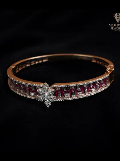 A sleek bangle featuring a channel of baguette-cut rubies, accented with a central diamond floral motif.
