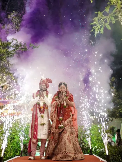 The couple greets their guests with folded hands, surrounded by purple smoke and cold pyro fireworks for a dramatic and welcoming entrance.