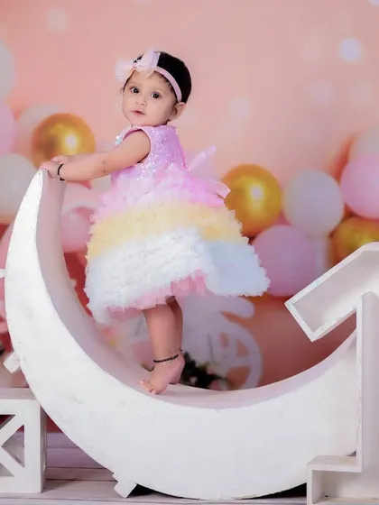 A beautiful first birthday portrait of a baby girl in a rainbow dress, standing on our moon prop with the number "1" beside her.