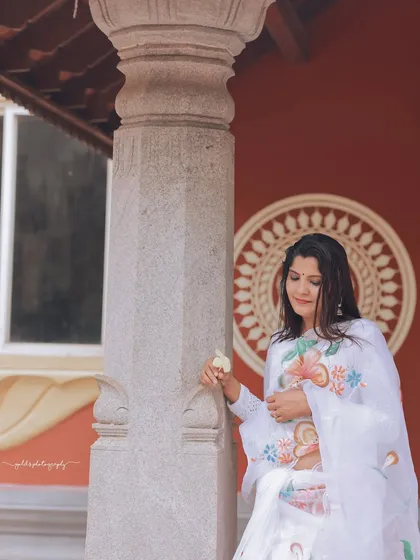A serene portrait with the bride standing by a pillar, the red wall and mandala painting in the background adding a pop of color and cultural significance.