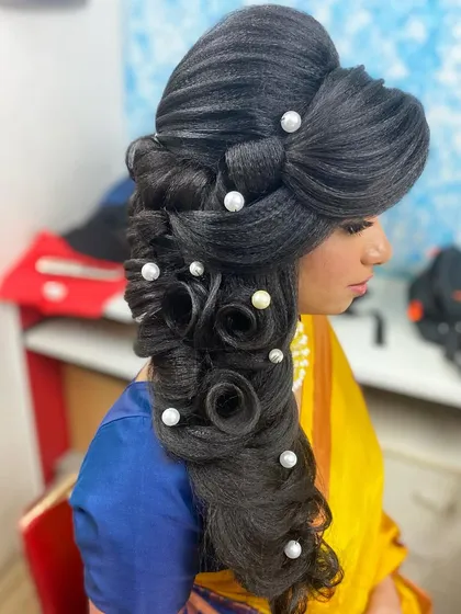 An elaborate hairstyle for a reception or grand event, featuring a cascade of curls and rolls embellished with pearls. This look is all about volume, texture, and glamour.
