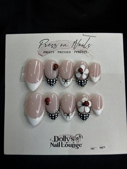 A cute and playful press-on set featuring a French manicure, polka dots, and 3D ladybug and bow details.