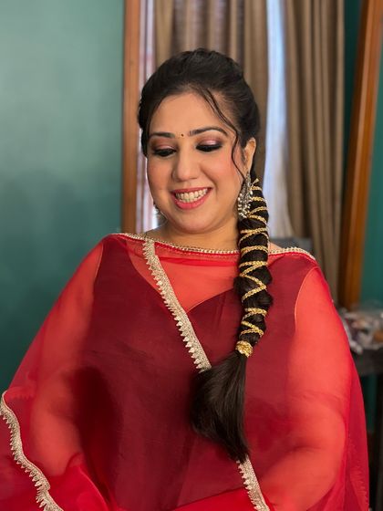 A client looking effortlessly chic in a red suit. The makeup features a classic black smokey eye and a nude lip, paired with a stylish braided hairstyle.