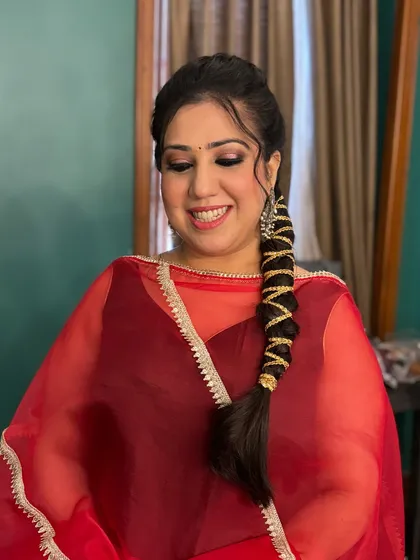 A client looking effortlessly chic in a red suit. The makeup features a classic black smokey eye and a nude lip, paired with a stylish braided hairstyle.