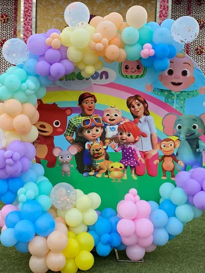 A circular Cocomelon backdrop surrounded by a rainbow of pastel balloons, featuring the entire cast of characters for a cheerful photo opportunity.
