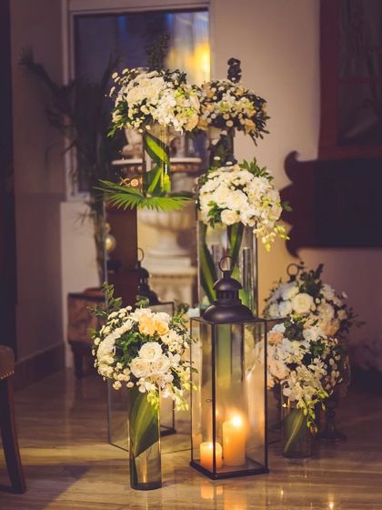 Creating a warm welcome with clusters of classic white floral arrangements and lanterns. The combination of soft candlelight and fresh flowers in tall glass vases provides a sophisticated and inviting ambiance for any gala.