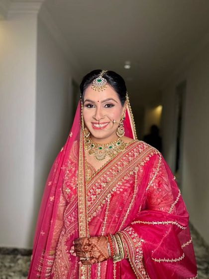 A happy, smiling client ready for a wedding. Her makeup is classic and radiant, with a beautiful pink lehenga.