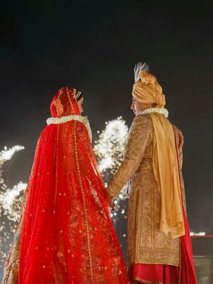 Amidst the grandeur of a palace wedding, it's the quiet moments that often resonate the most. Here, the couple shares a private glance as fireworks light up their new beginning, a perfect blend of spectacle and intimacy.
