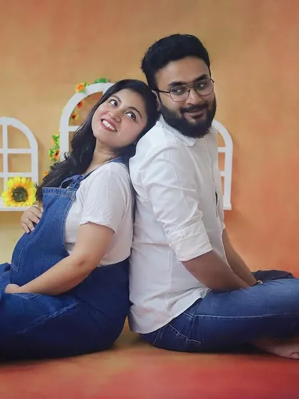 A cozy and cute couple's portrait. The denim overalls and the warm, sunny backdrop in the studio create a cheerful and relaxed atmosphere for this maternity shoot.