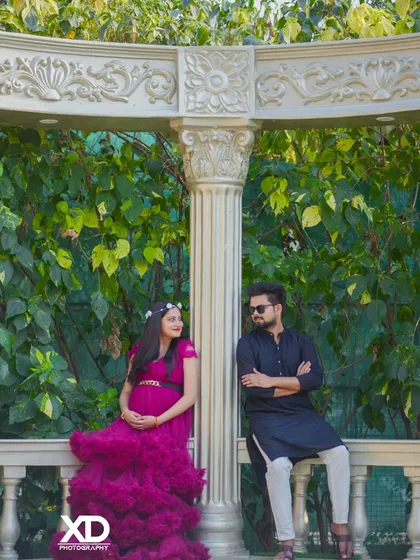 A relaxed portrait of a couple leaning against a white balustrade in a garden setting.