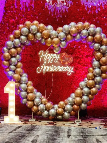 A perfect photo booth for a first anniversary celebration. This large heart-shaped arch is made of silver and gold chrome balloons, with a 'Happy Anniversary' neon sign and a light-up number '1' to mark the special milestone.
