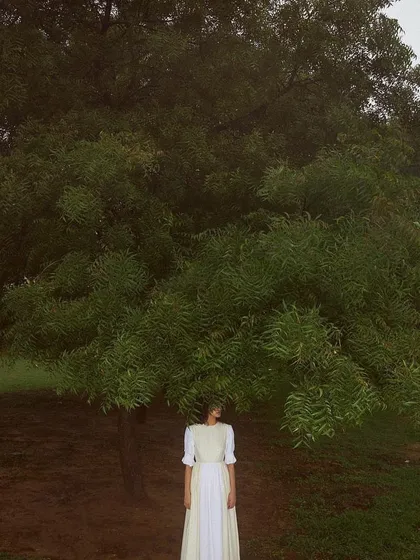 A wide shot from the Sruti Dalmia campaign, placing a model in a simple white dress beneath a large, sprawling tree. The styling and composition create a sense of scale and connection to nature, resulting in a peaceful and poetic image.