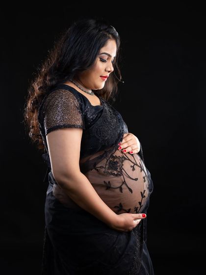A classic and elegant portrait. This mom-to-be cradles her bump, her form beautifully highlighted in a sheer black embroidered saree against a dark background.