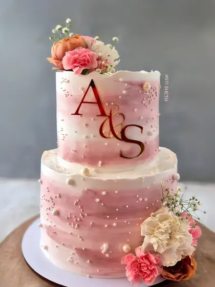 A two-tiered anniversary cake in a rustic pink ombre style. This 3kg rich chocolate cake is decorated with fresh florals and pearls.