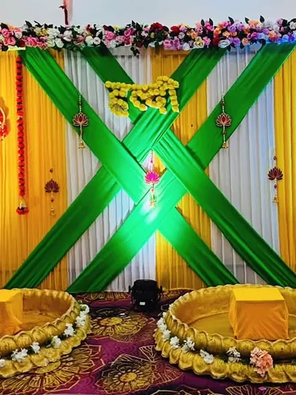 For a grander celebration, I designed this elaborate stage with crisscrossing green drapes over a yellow and white base. The two large brass urlis provide traditional seating for the couple, making it a stunning focal point.