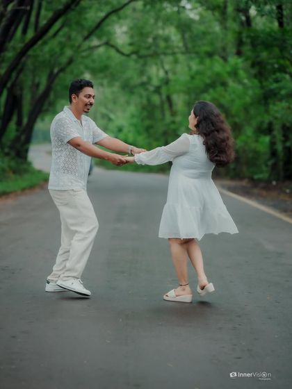 The couple holds hands and twirls on an empty road, surrounded by nature. Their laughter and motion create a dynamic and happy pre-wedding photograph.