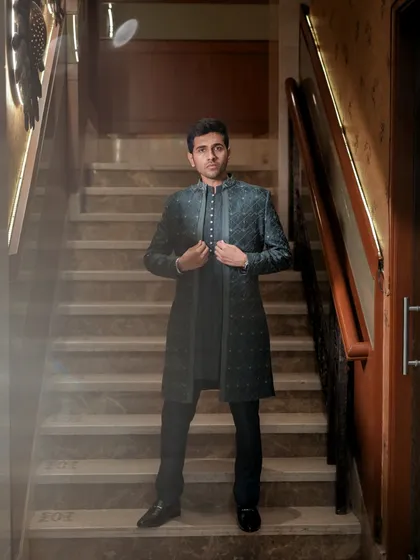 A dramatic groom portrait on a staircase, with soft, smoky light adding to the mood. This shot showcases his stylish dark teal sherwani and confident pose.