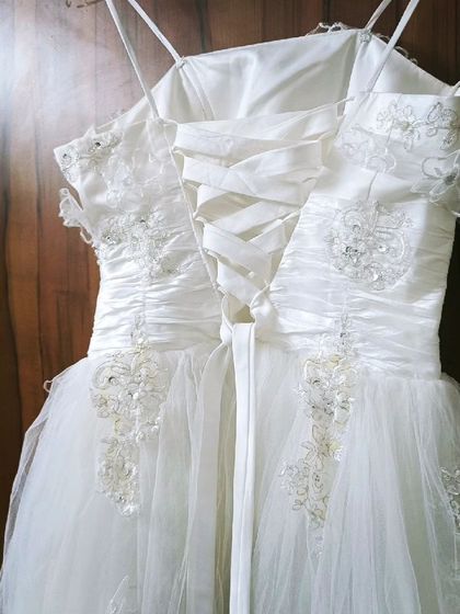 A close-up of the back of a white corset-style gown. The lace-up detail allows for an adjustable fit, and the bodice is adorned with delicate beading and embroidery.