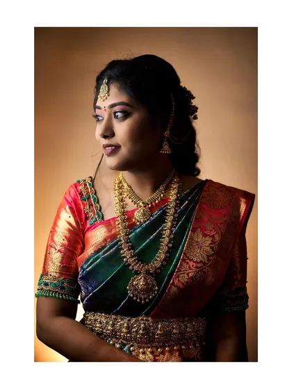 A classic portrait of a bride from her ring ceremony. The warm studio lighting enhances the rich colors of her multi-toned silk saree and heavy gold jewellery.