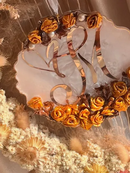 A detailed shot of the custom logo on the hanging wreath. The preserved golden roses beautifully frame the couple's initials, making it a truly personal piece.