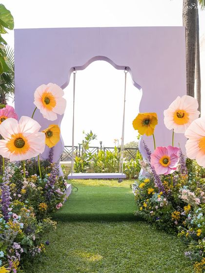 A lavender-colored arch frames a swing, surrounded by oversized paper poppies, creating a dreamy photo opportunity.