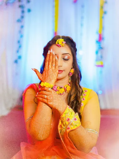 An artistic portrait of the bride during her Mehendi ceremony. The pose, with one hand gently covering her eye, is both playful and elegant, drawing attention to the beautiful henna.