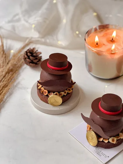 A dapper entremet dessert for Father's Day, shaped with a chocolate hat and mustache. This sophisticated dessert features layers of espresso mousse, caramel, and hazelnut praline.
