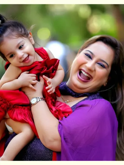A mother and daughter sharing a laugh during an outdoor portrait session. Their vibrant outfits pop against the natural green background.