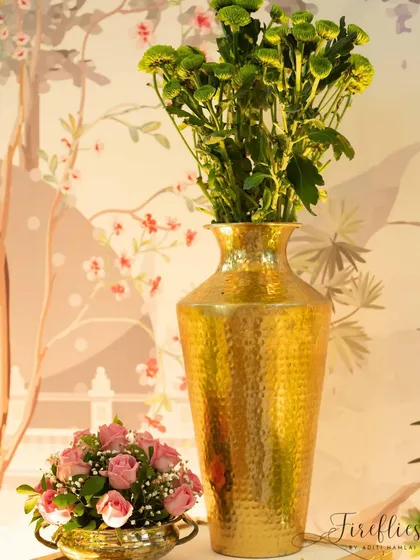 A detail shot of a brass vase with pink roses, set against the custom botanical wallpaper of the 'Shrimant' ceremony.