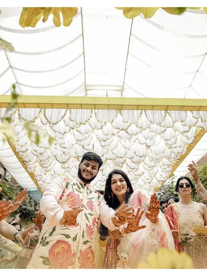 The couple shows off their henna-covered hands, surrounded by their loved ones under a beautiful floral canopy during their Haldi ceremony.
