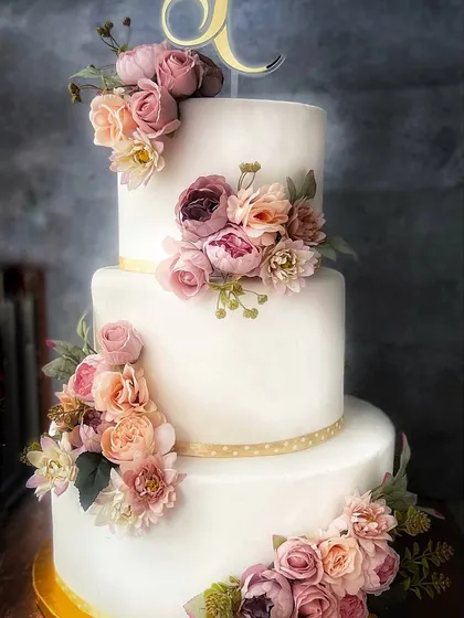 A full view of the magnificent three-tier wedding cake, adorned with a cascading arrangement of delicate, handcrafted sugar flowers.