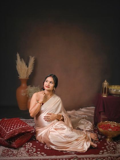 A serene portrait featuring a lustrous satin saree. The earthy props like clay pots and pampas grass create a rustic yet elegant traditional setting.