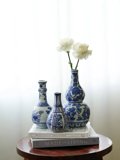 A collection of blue and white ceramic vases styled on a wooden stool against a bright window. The clean, high-key lighting gives this shot a serene and airy feel, perfect for minimalist home decor.