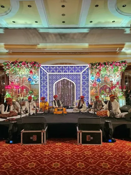 A full stage setup for a Sufi music night, featuring a backdrop with traditional blue and white tile patterns, framed by vibrant floral arrangements.